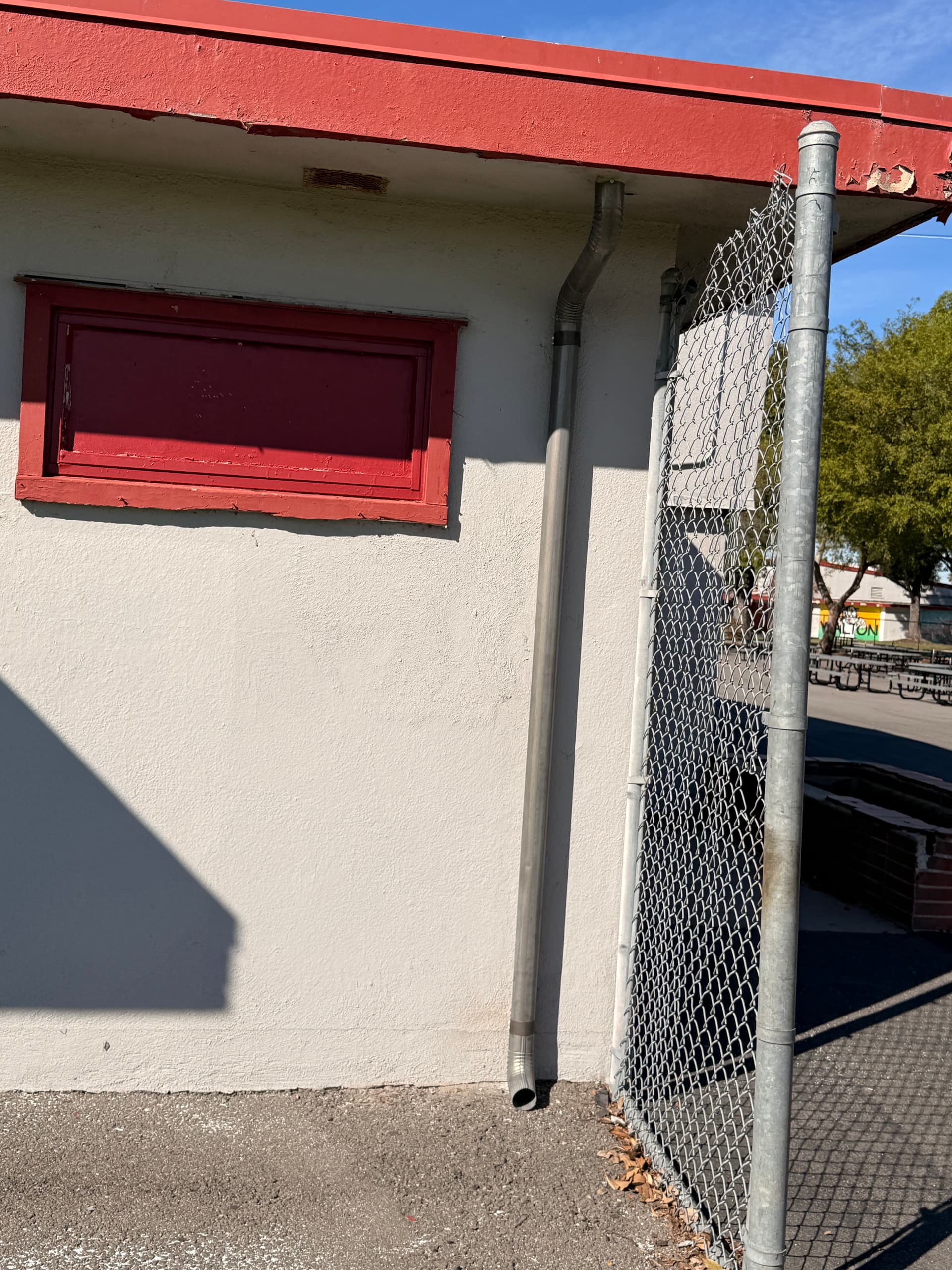 Repaired gutter downspout connection and pipe run along stucco building wall
