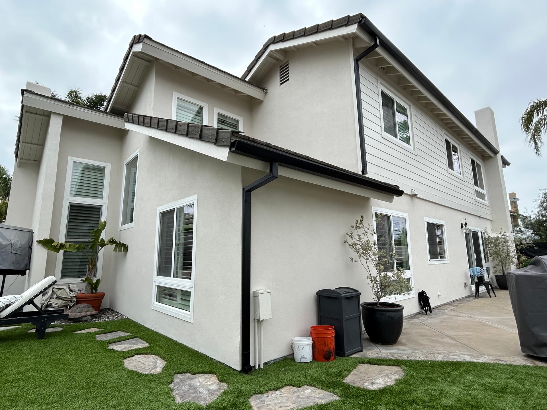 Completed dark seamless gutter system on a two-story stucco home with backyard view