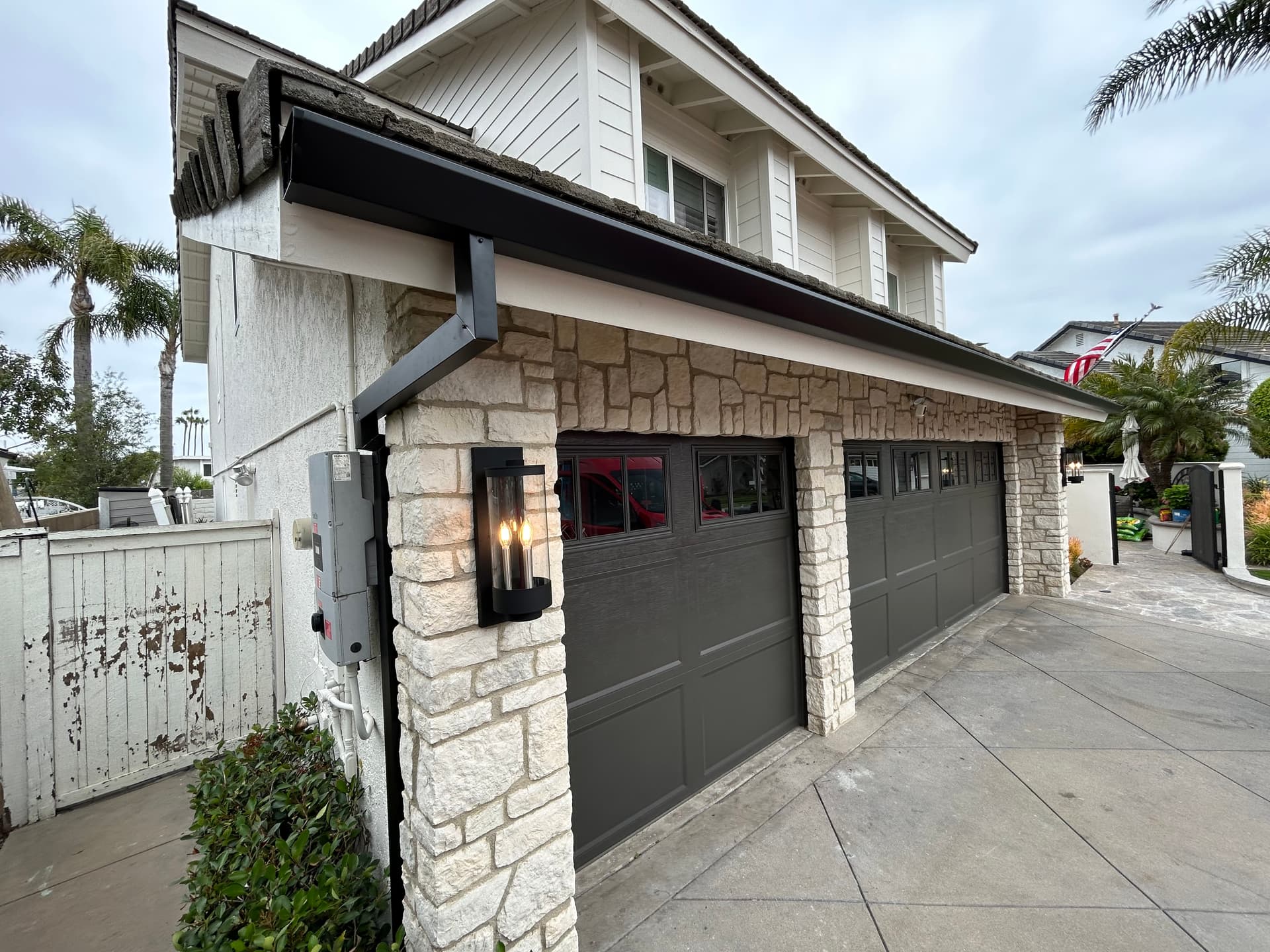 Black seamless gutter and downspout on a two-story stone and stucco home with garage