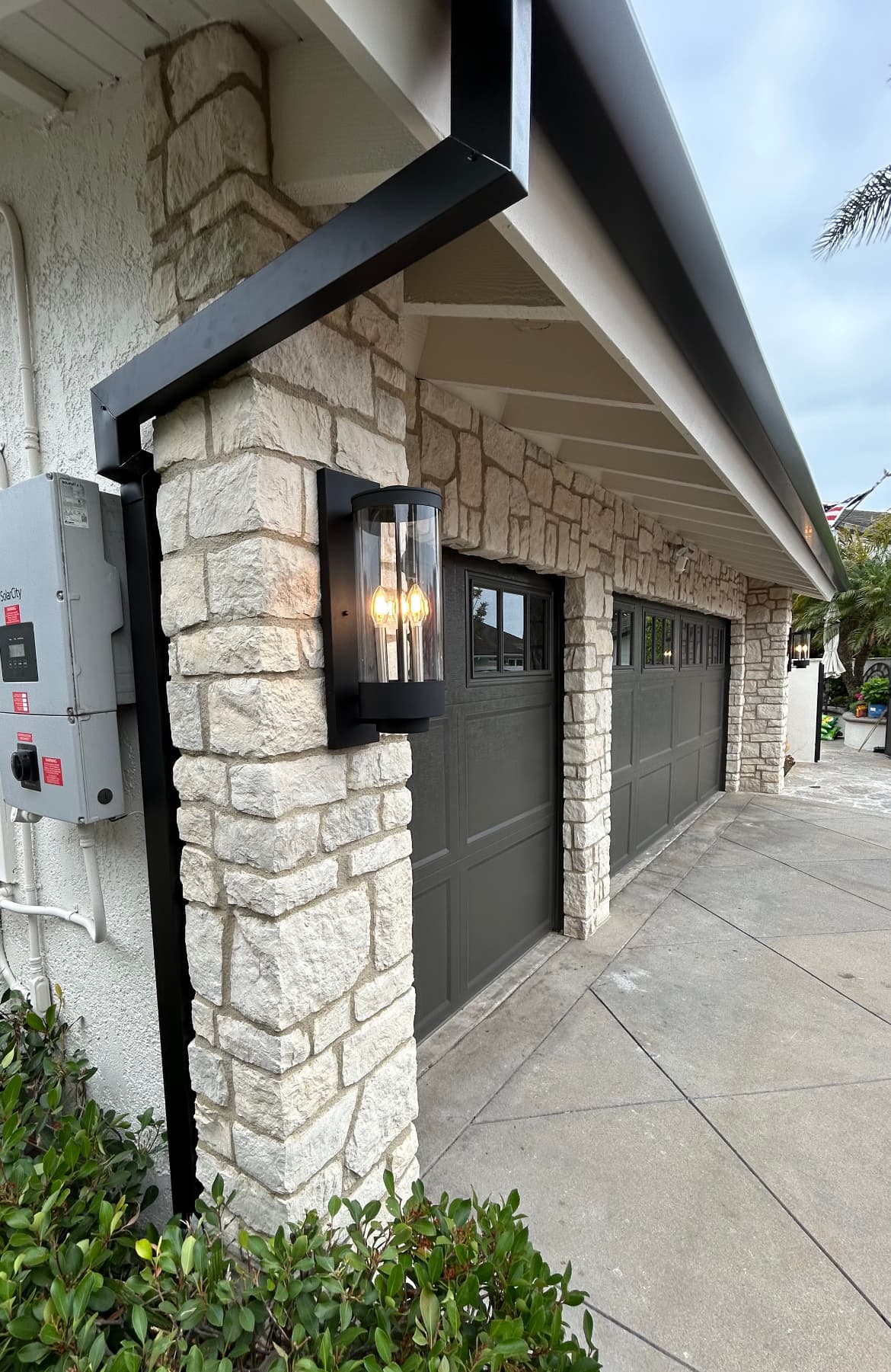 Black seamless gutter and square downspout on a stone-front garage close-up
