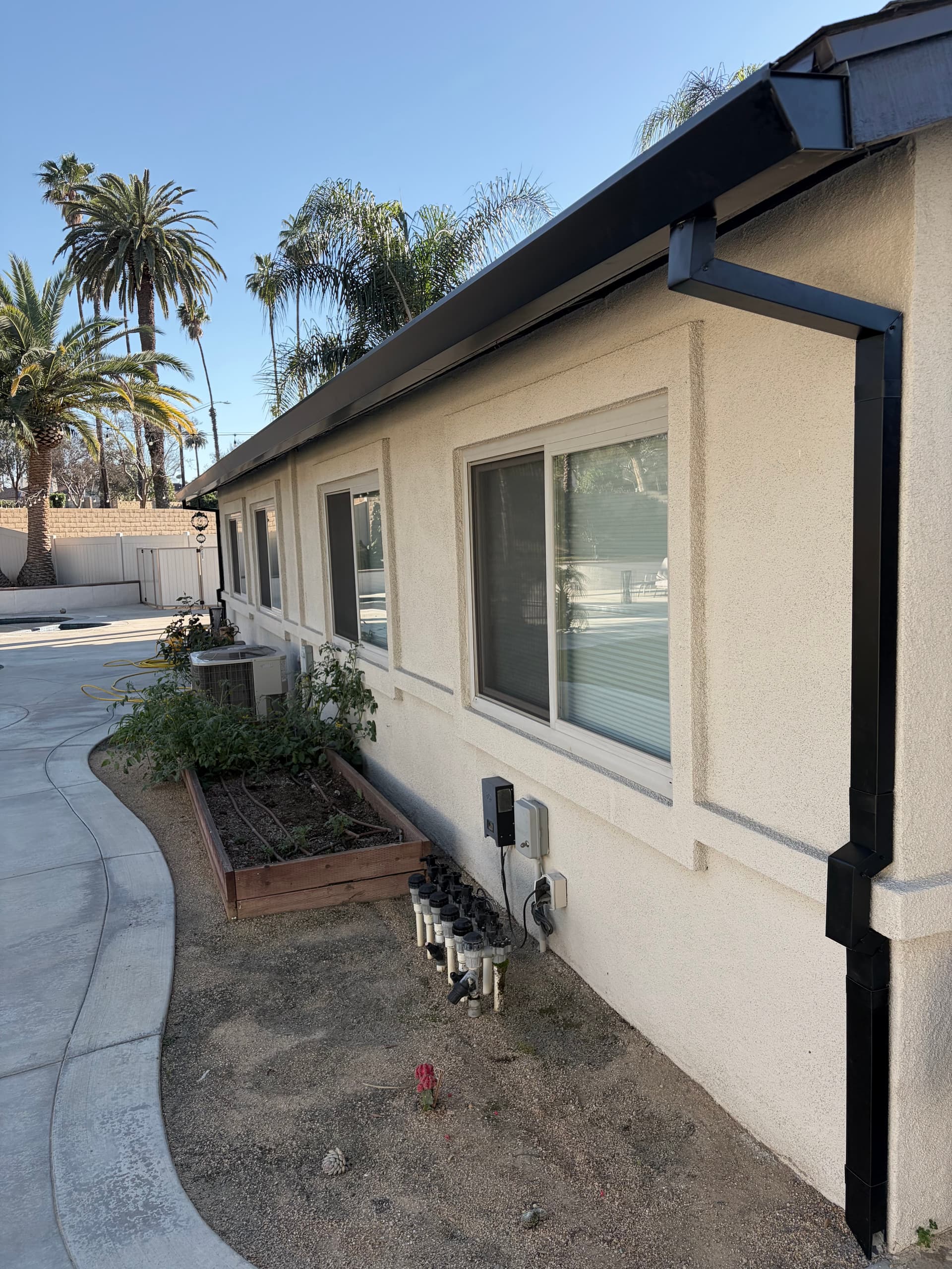 Dark seamless gutter on a single-story stucco home with palm trees