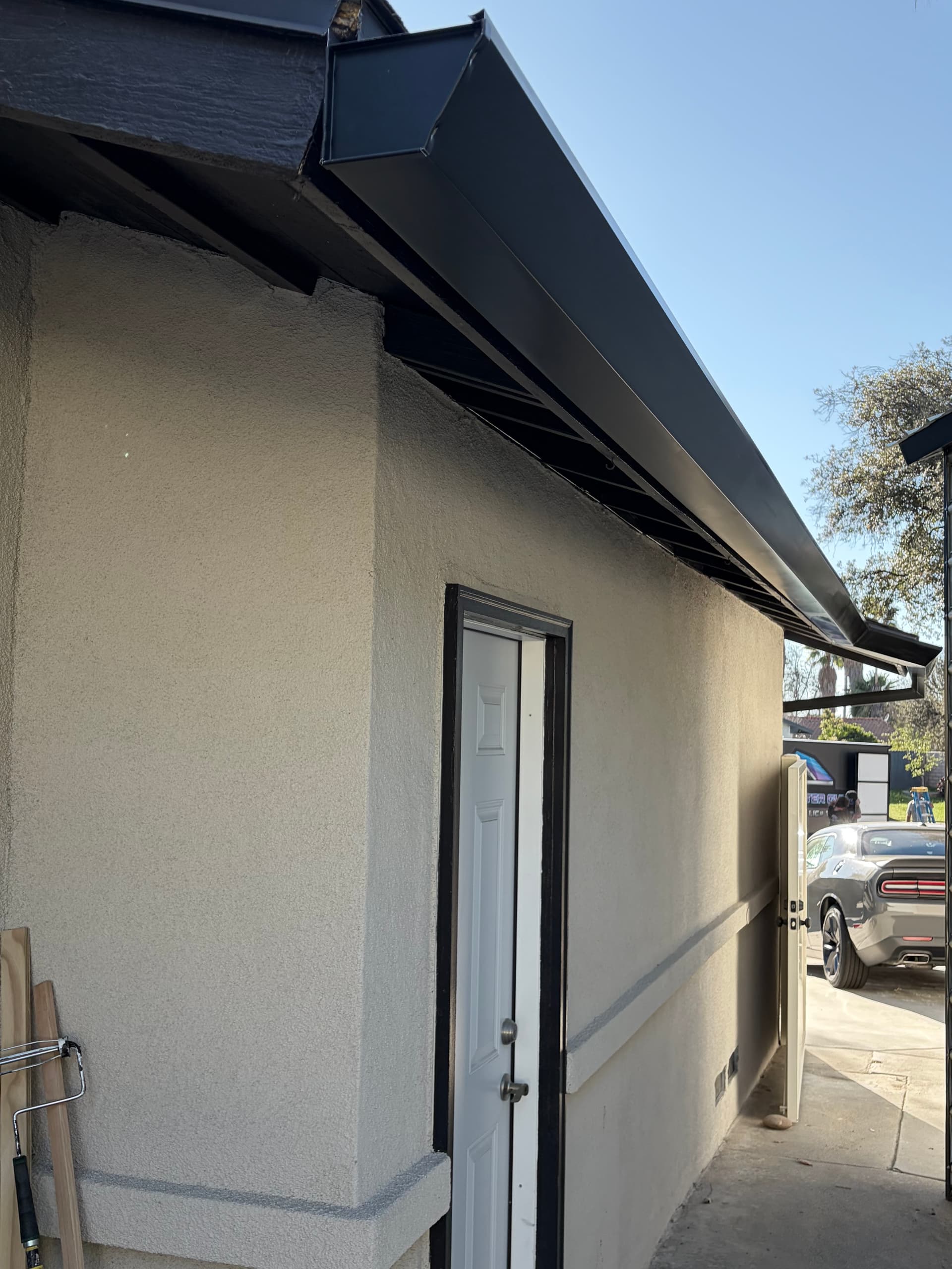 Black seamless gutter running along a stucco home with close-up of gutter profile