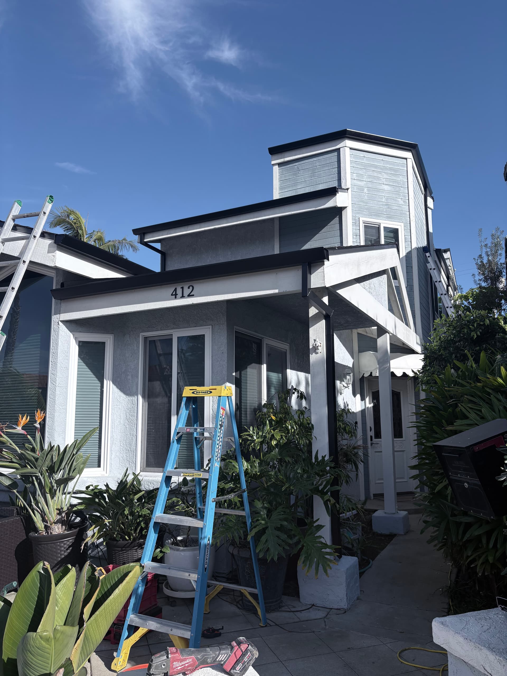 Dark seamless gutter installation with crew and ladder on a gray craftsman home